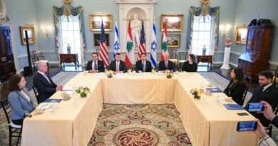 People are seated around a large U-shaped table in front of American, Israeli, and Lebanese flags.