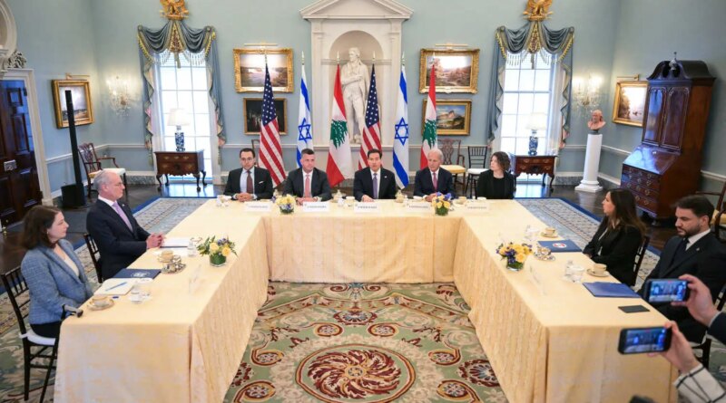 People are seated around a large U-shaped table in front of American, Israeli, and Lebanese flags.