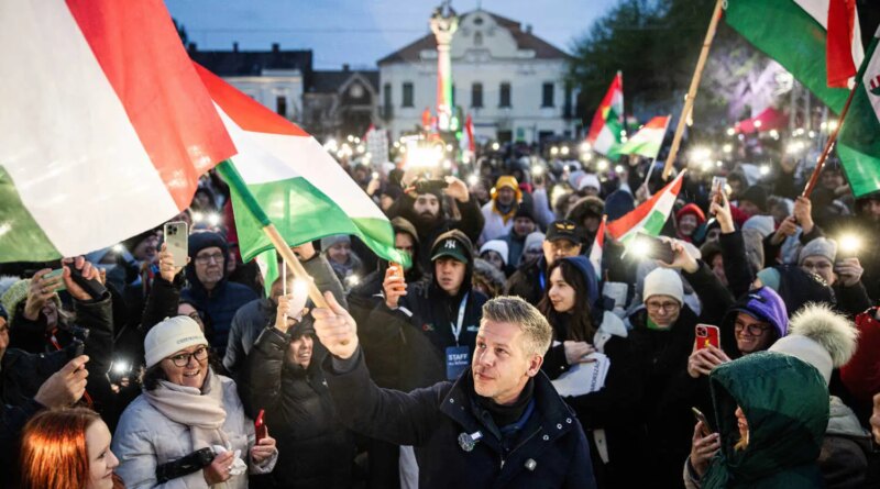 Peter Magyar stands at the head of a large crowd of people, many holding Hungarian flags, in an outdoor setting with buildings in the background.