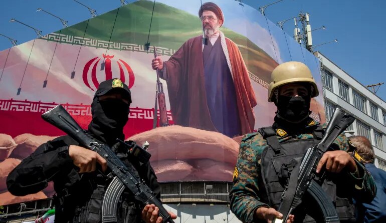 TEHRAN, IRAN - APRIL 9: Members of the Iranian security forces stand guard under a large portrait of Iran's new Supreme Leader, Mojtaba Khamenei, during a memorial to mark the 40th day since his father, Ali Ayatollah Khamenei, was killed in US-Israeli joint strikes, on April 9, 2026 in Tehran, Iran. On April 8 President Donald Trump announced a two-week ceasefire between the US and Iran, conditional on shipping being allowed to resume through the Strait of Hormuz. (Photo by Majid Saeedi/Getty Images)