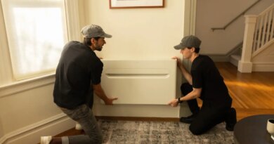 Two men install a heat pump on a wall.