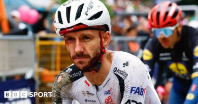 Adam Yates in a torn cycling kit and helmet, both predominantly white