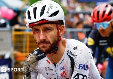 Adam Yates in a torn cycling kit and helmet, both predominantly white