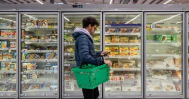 Man standing in front of refrigerator cases at a supermarket.
