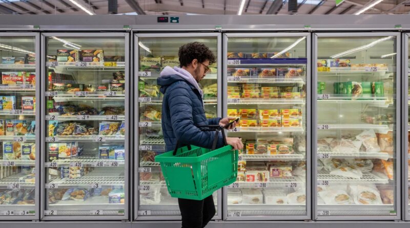 Man standing in front of refrigerator cases at a supermarket.
