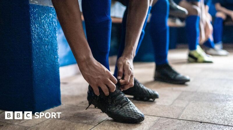 Soccer player tying shoelaces while preparing for match in the locker room