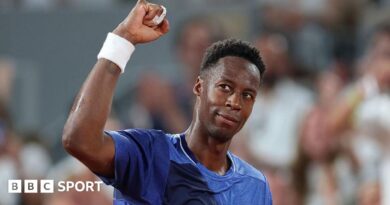Gael Monfils, wearing a blue t-shirt, looks up to his right and raises his right fist