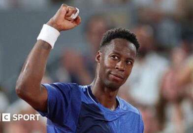 Gael Monfils, wearing a blue t-shirt, looks up to his right and raises his right fist