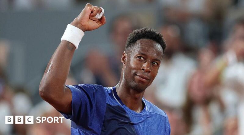 Gael Monfils, wearing a blue t-shirt, looks up to his right and raises his right fist