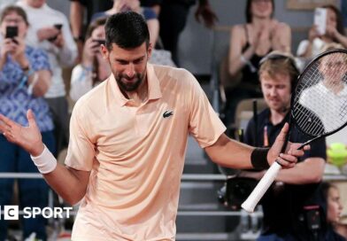 Novak Djokovic, wearing a peach polo shirt, dances with his racquet in his left hand