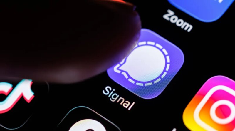 The Signal app logo can be seen on the display of a smartphone while a finger taps on the application icon.