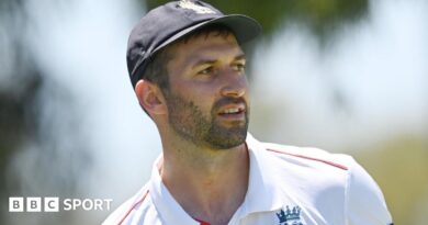 Mark Wood, wearing a blue England cap, looks to the side