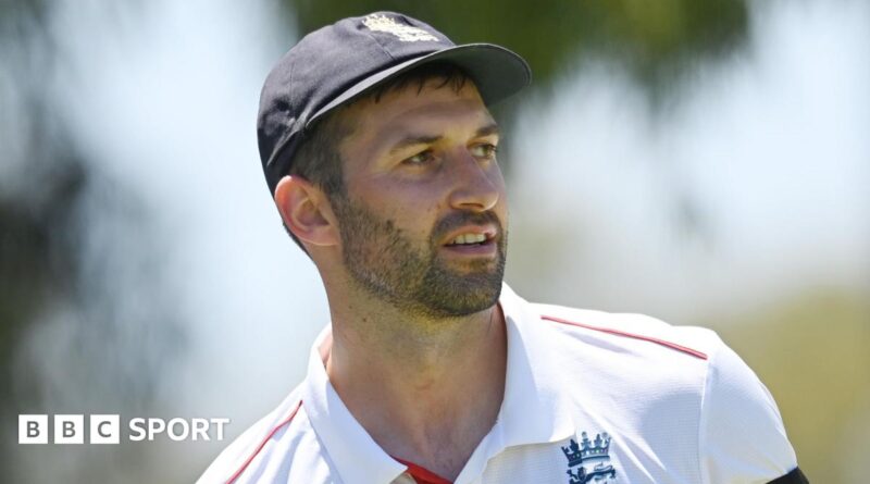 Mark Wood, wearing a blue England cap, looks to the side