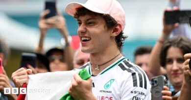 Kimi Antonelli celebrates his race win in Miami while holding the Italian flag. A crowd are gathered around him and taking photographs