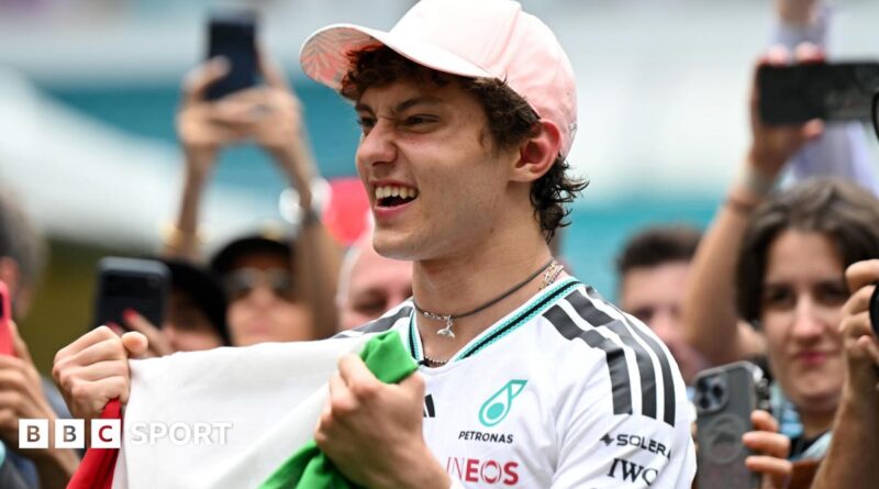 Kimi Antonelli celebrates his race win in Miami while holding the Italian flag. A crowd are gathered around him and taking photographs