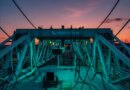 A drilling rig stands in front of a sunset.