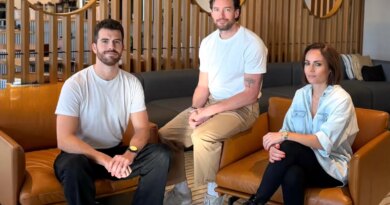 Two men and a woman sit on leather chairs in a well appointed office space.
