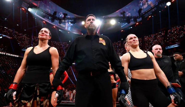 INGLEWOOD, CALIFORNIA - MAY 16: Gina Carano and Ronda Rousey stand with referee John McCarthy after their featherweight bout during the main card of Netflix's Ronda Rousey vs. Gina Carano at Intuit Dome on May 16, 2026 in Inglewood, California. Sarah Stier/Getty Images for Netflix/AFP (Photo by Sarah Stier / GETTY IMAGES NORTH AMERICA / Getty Images via AFP)