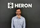 Drew Baglino standing in front of the Heron Power logo.