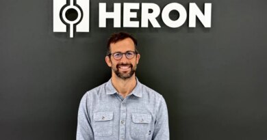 Drew Baglino standing in front of the Heron Power logo.