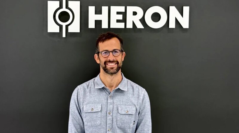 Drew Baglino standing in front of the Heron Power logo.