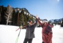 Two friends high-fiving while skiing.