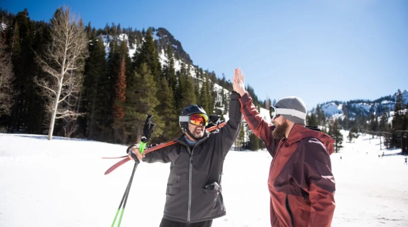 Two friends high-fiving while skiing.