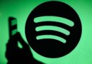 The Spotify logo displays on a screen with a person holding a phone.