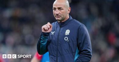 Steve Borthwick, wearing a nany blue zip-up England jacket, looks into the distance, his right hand raised to shoulder level