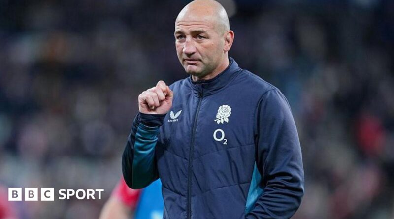 Steve Borthwick, wearing a nany blue zip-up England jacket, looks into the distance, his right hand raised to shoulder level