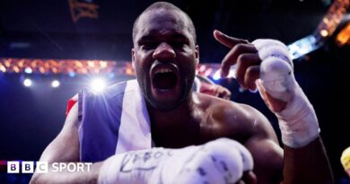 Daniel Dubois leans over the ropes of a boxing ring and holds up his hand