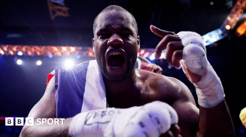 Daniel Dubois leans over the ropes of a boxing ring and holds up his hand