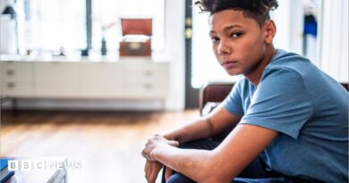 An anxious-looking teenager sits in a room, looking at the camera. 