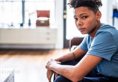 An anxious-looking teenager sits in a room, looking at the camera. 