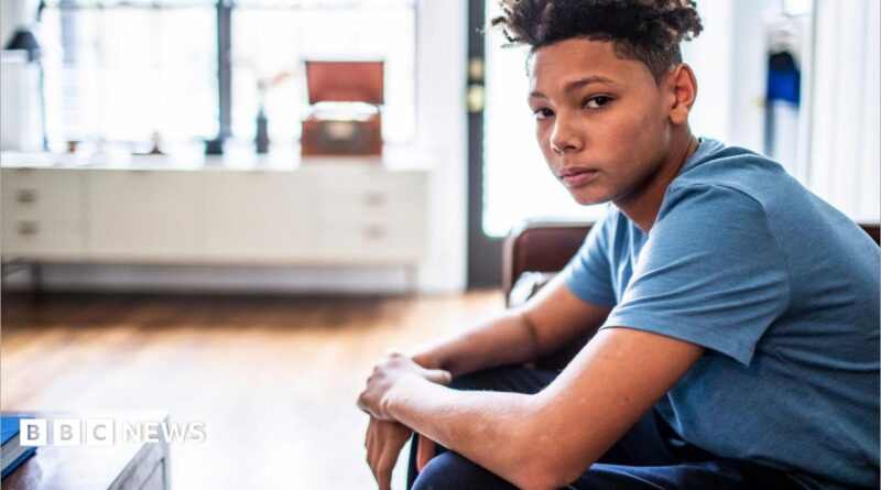 An anxious-looking teenager sits in a room, looking at the camera.
