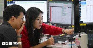 A woman in a red cardigan points to a screen during a discussion with a colleague in a trading room in Seoul 