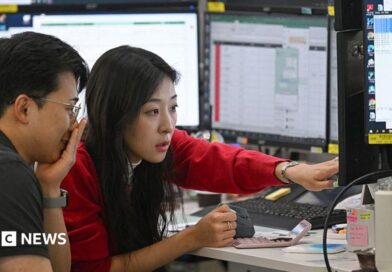 A woman in a red cardigan points to a screen during a discussion with a colleague in a trading room in Seoul 
