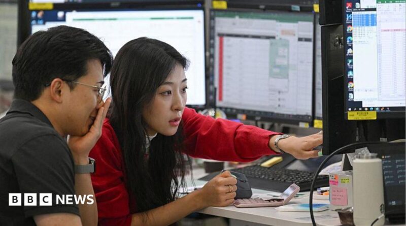 A woman in a red cardigan points to a screen during a discussion with a colleague in a trading room in Seoul