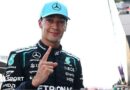 George Russell looks at the camera and points his index figure upwards