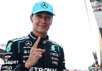 George Russell looks at the camera and points his index figure upwards