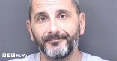 A custody shot of Matthew Ashley Foster-Smith. He has short hair and a beard and is wearing a grey jumper.