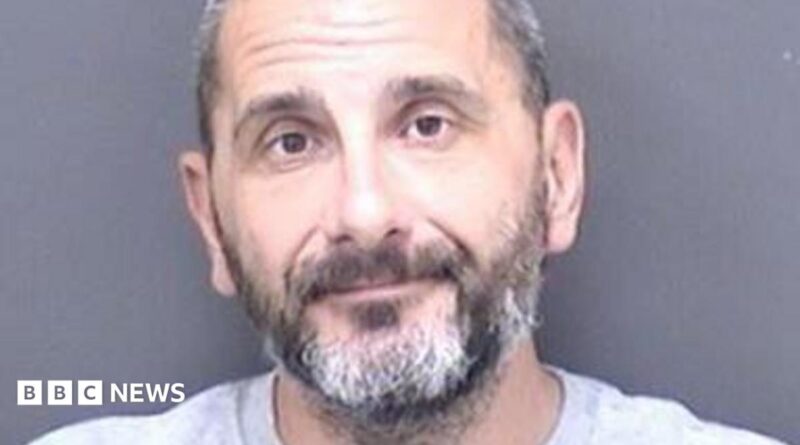 A custody shot of Matthew Ashley Foster-Smith. He has short hair and a beard and is wearing a grey jumper.