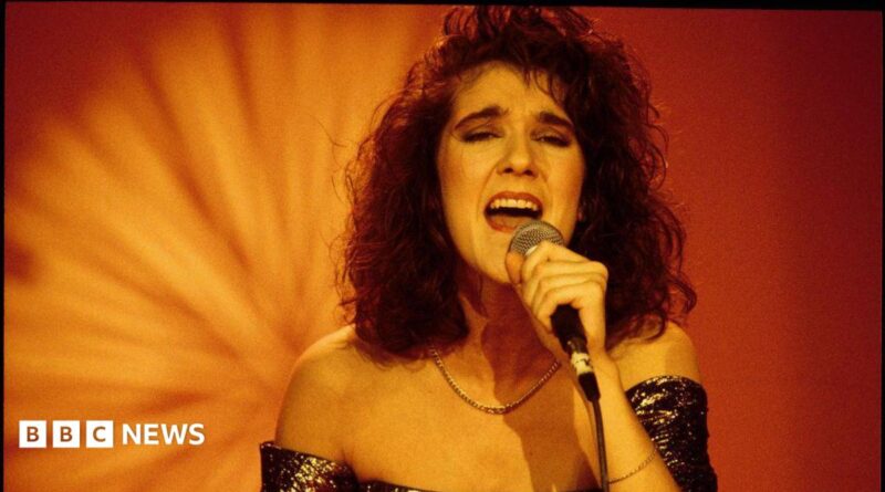 A young Celine Dion sings while holding a microphone. She is wearing a glittery strapless dress.