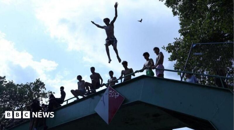 A person jumps off a bridge into the Canal Saint-Martin as public swimming having been allowed earlier on part of it due to rising of temperatures