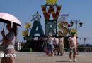 A woman walks under an umbrella past a "Warsaw" sign as a heatwave sweeps Poland, in Warsaw, Poland, 