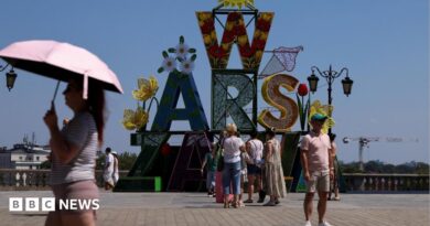A woman walks under an umbrella past a "Warsaw" sign as a heatwave sweeps Poland, in Warsaw, Poland, 