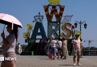 A woman walks under an umbrella past a "Warsaw" sign as a heatwave sweeps Poland, in Warsaw, Poland, 