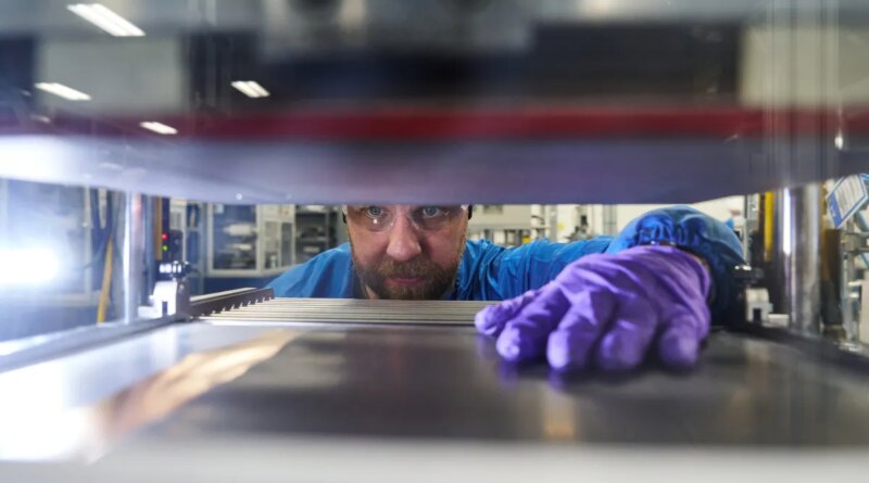 A man reaches his hand into a machine to grab a battery prototype.