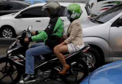 A Gojek driver pillions a customer as he rides his motorcycle through a business district street in Jakarta
