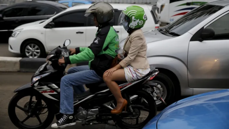 A Gojek driver pillions a customer as he rides his motorcycle through a business district street in Jakarta